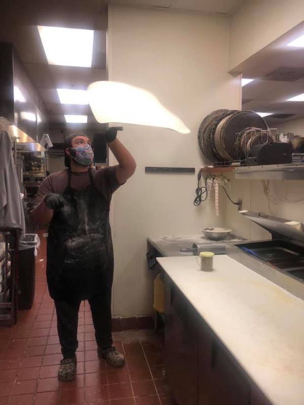 A man in an apron spinning dough. 