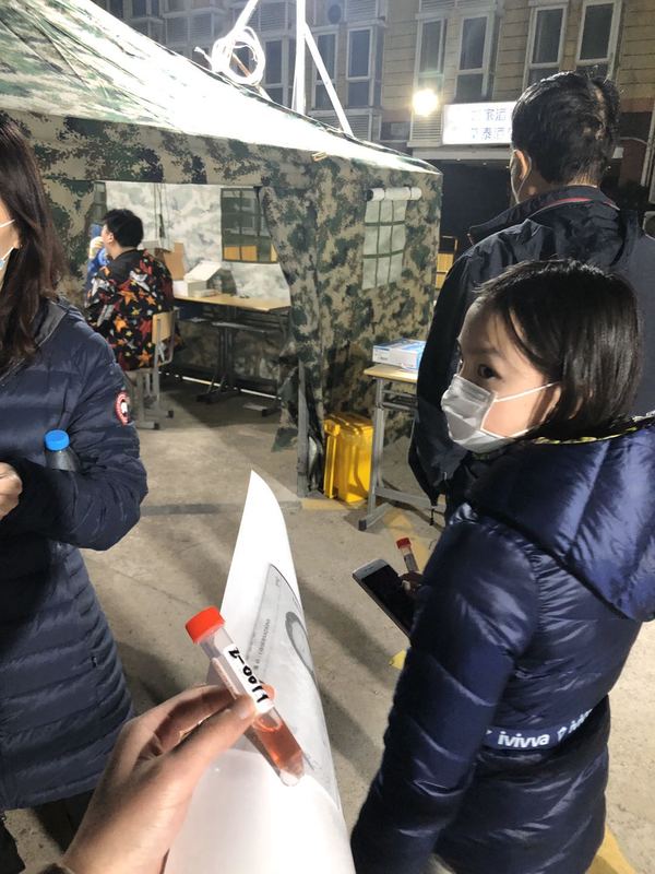 A test tube with pinkish colored liquid in it being held by the photographer, that are also other people holding test tubes with pinkish colored liquid in it.