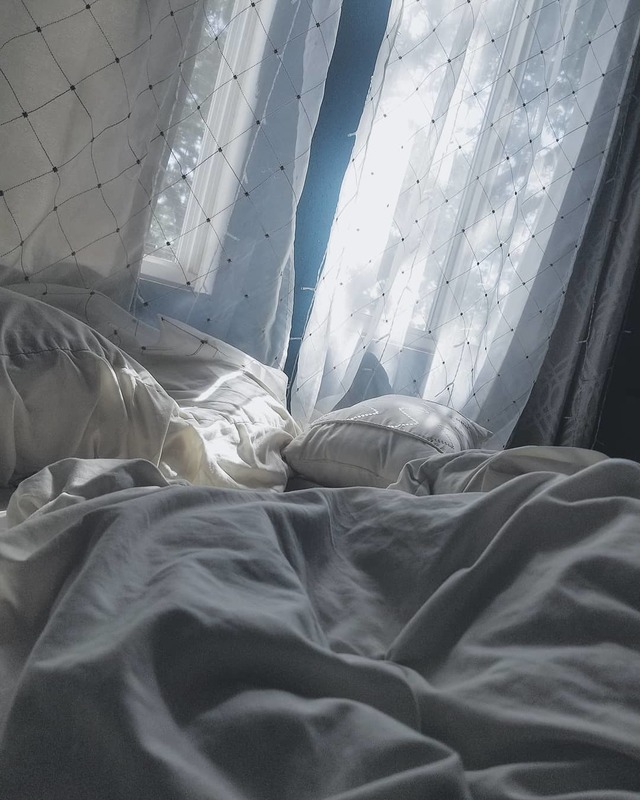 an unmade bed with gray comforter and white pillows