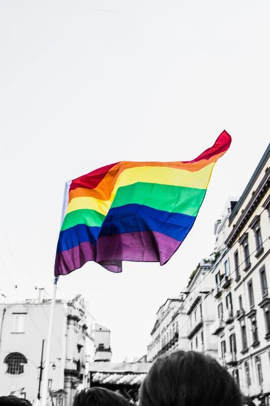 This is a picture of a group of people flying a rainbow pride flag in the street.