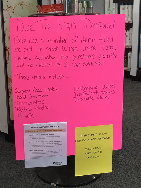 A bright pink sign discussing the high demand of certain products and limiting those products to only 1 per customer. Those products are: surgical face masks, hand sanitizer, thermometers, rubbing alcohol, aloe vera, antibacterial wipes, disinfectant sprays, disposable gloves. On the bottom right is a yellow paper sign attached to the pink sign saying: OTHER ITEMS THAT ARE LIMITED TO 1 PER CUSTOMER TOILET PAPER, PAPER TOWELS, HAND SOAP.