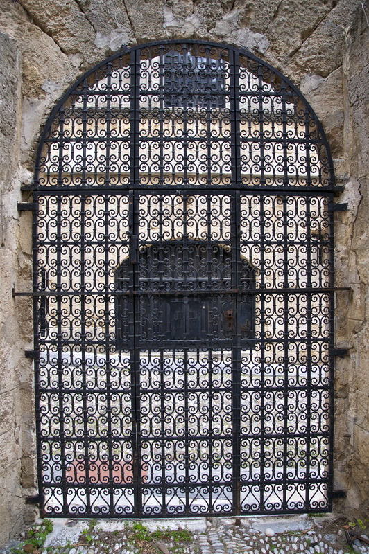 This is a picture taken of an ornate iron gate that has been installed in a stone archway. 