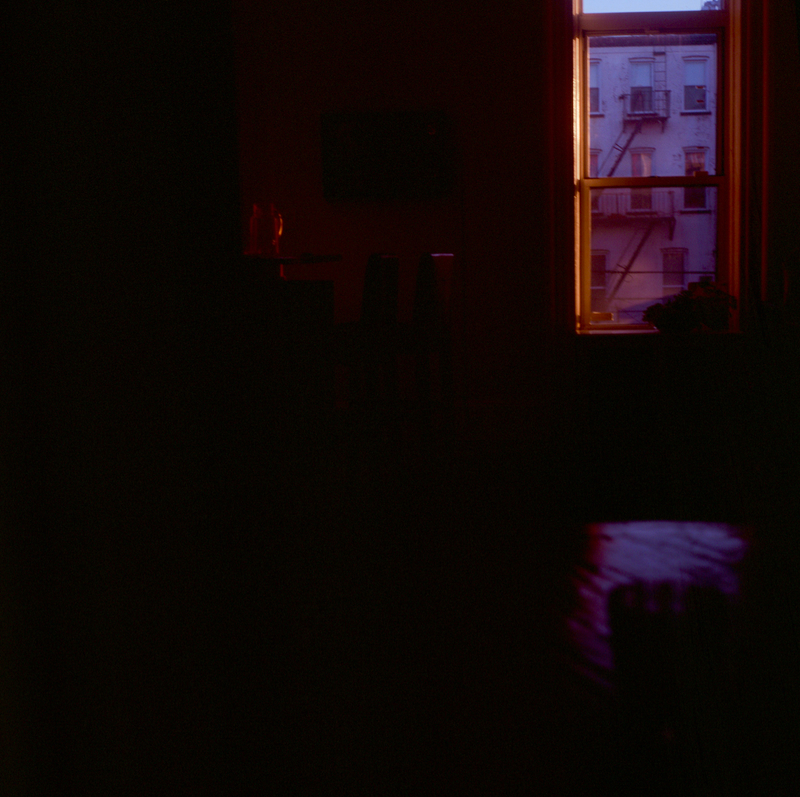 A picture of a dark bedroom from the inside, with a window in the foreground showing the first light of dawn.