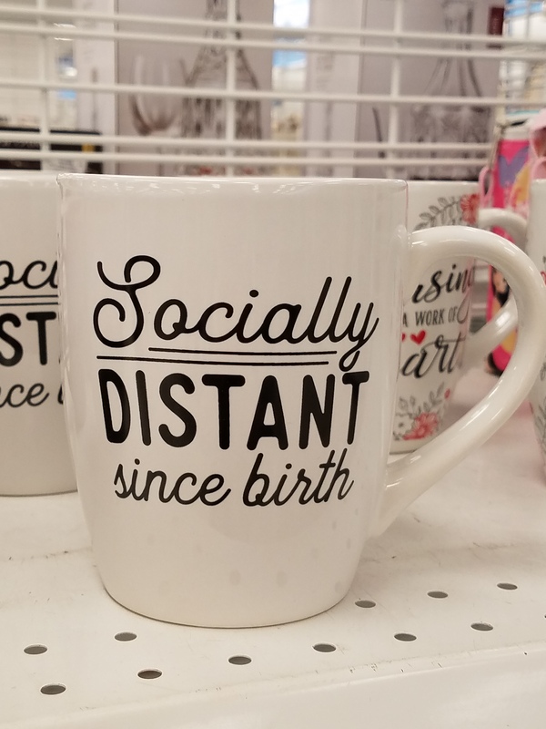 This is a picture of a coffee mug which has the message "Socially distant since birth" written in cursive on it.