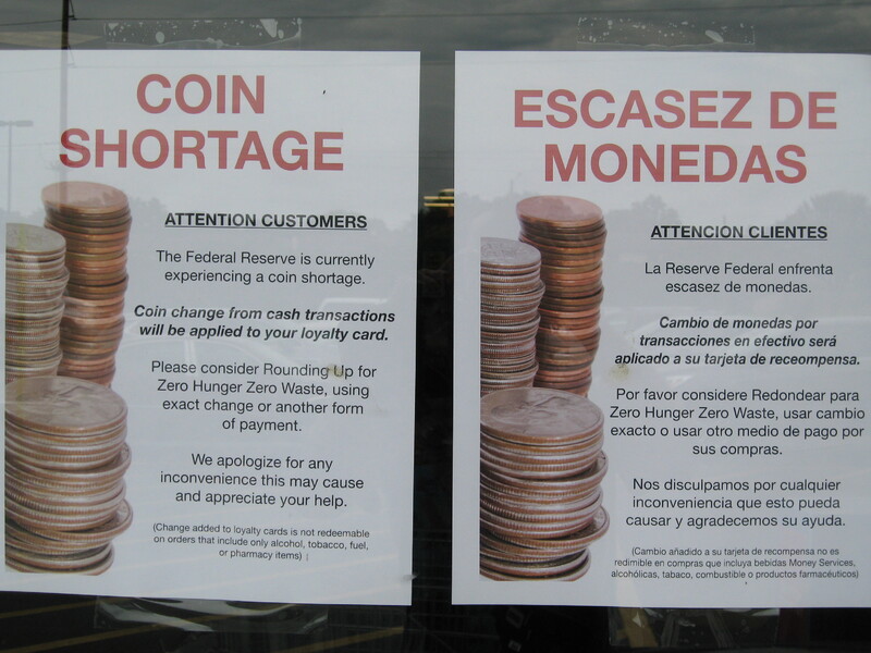 Two signs, one in Spanish and one in English, detailing a coin shortage.