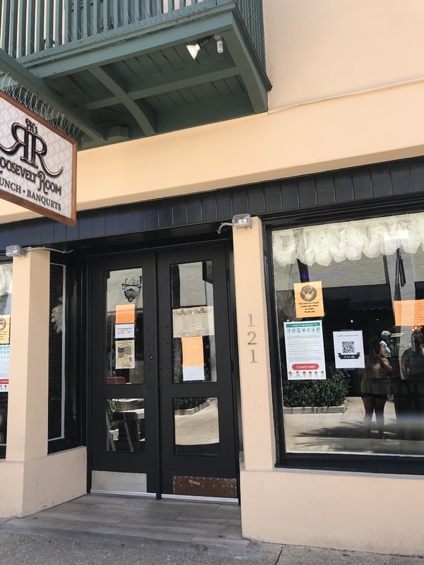 This is a picture taken of the entrance to a restaurant, which has many flyers in the window likely pertaining to COVID-19 policies.