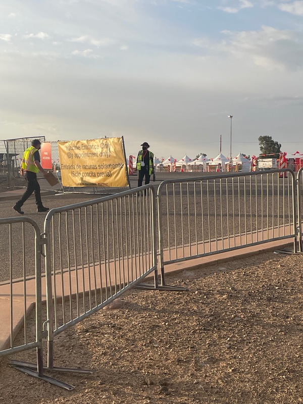 This is an image of volunteer COVID-19 vaccination workers preparing a parking lot to receive people to vaccinate. A sign out front says 'Vaccine Entrance Only (By appointment only)" in English and Spanish.