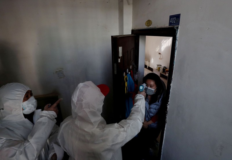 Two people in white gear scan temperature of woman in doorway.