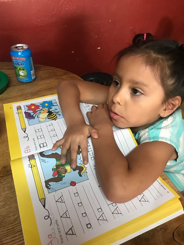 This is a picture of a young girl resting her elbows on her spelling homework, which lays on the table in front of her.