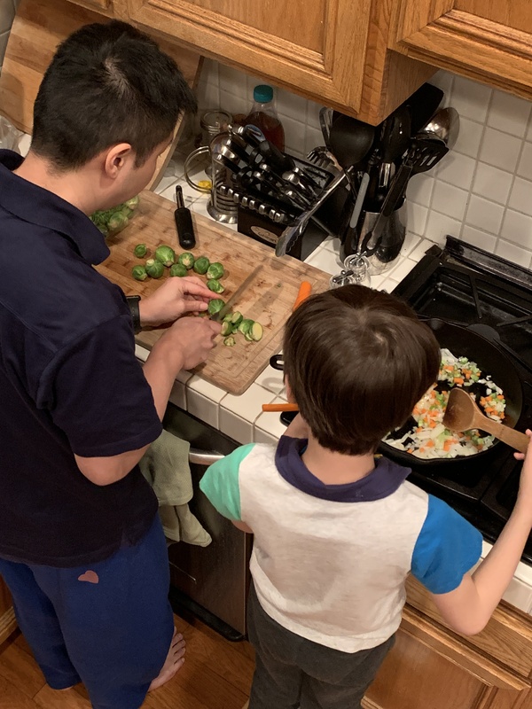 This is a picture of a man and his young son preparing dinner at a stove.