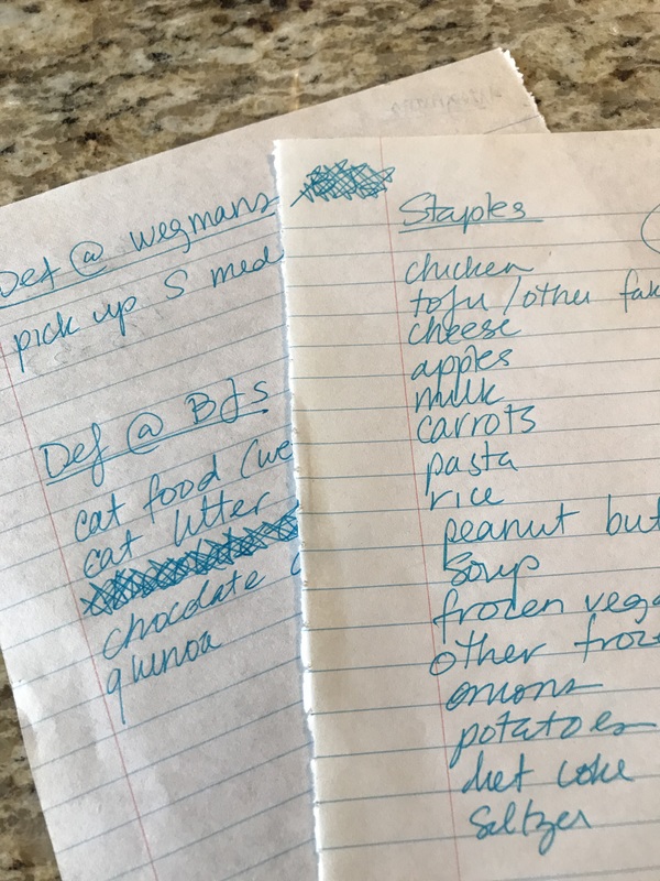 Two pieces of notebook paper with lists written on it about grocery and household essentials.
