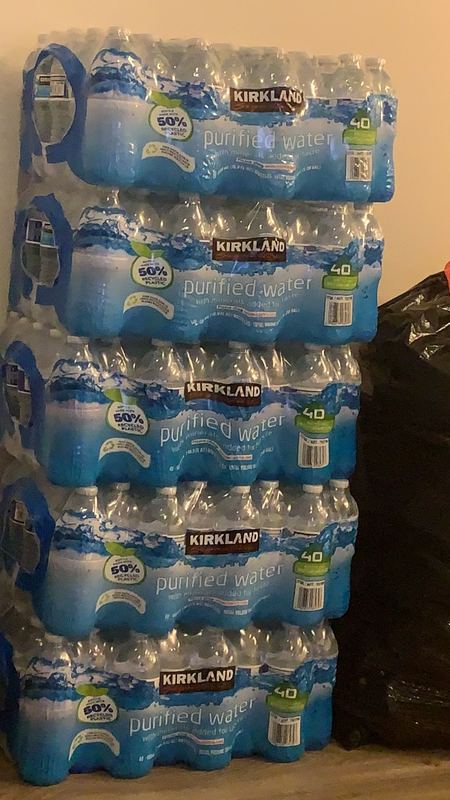 Six packs of Kirkland bottled water is stacked up against a wall.
