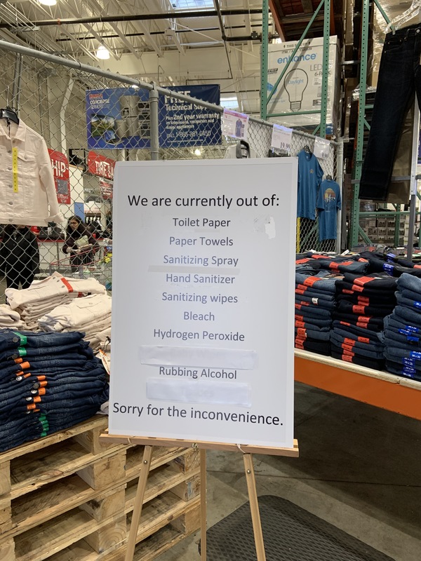 A white paper sign is propped up on a wooden stand that says: We are currently out of: Toilet Paper, Paper Towels, Sanitizing Spray, Hand Sanitizer, Sanitizing Wipes, Bleach, Hydrogen Peroxide, Rubbing Alcohol. Sorry for the inconvenience.