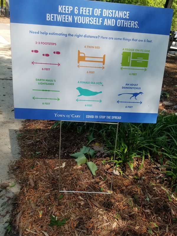 A blue sign that reads "keep 6 feet of distance between yourself and others".