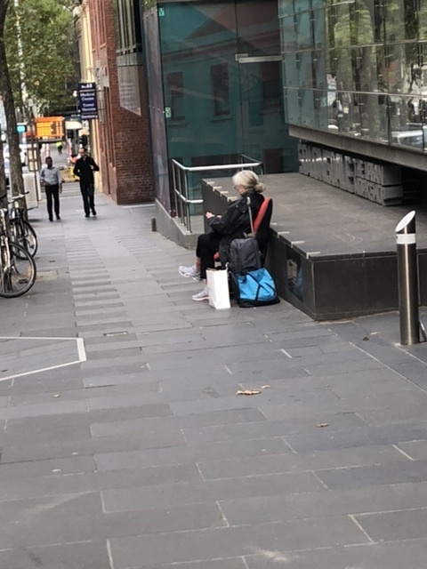 A sidewalk that has a woman sitting on a bench on her phone.