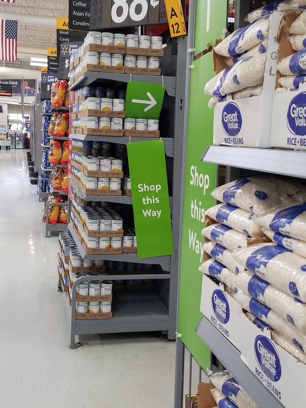 This is a picture taken of an aisle in a store, where a green sign is posted at the entrance reading "Shop this way".