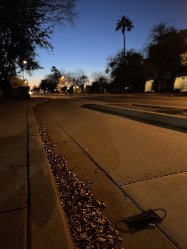 This is a picture taken of a discarded cloth face mask resting on a city street as the sun sets in the background. 