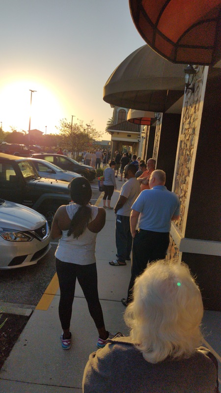 A long line of people are waiting outside of a grocery store.