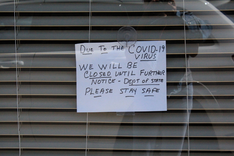 A business window with a hand written note in the window that says "Due to the COVID-19 virus we will be closed until further notice-Dept of State-Please stay safe."