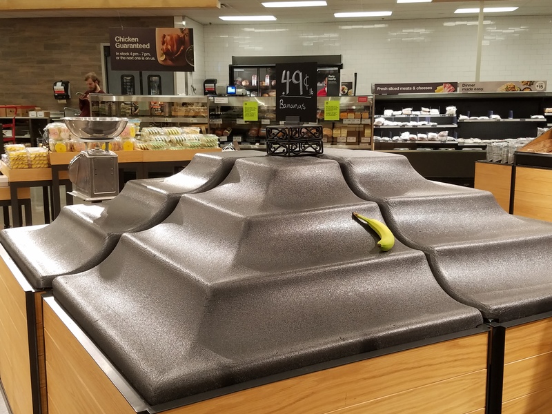 A grocery store has empty display with only one banana left. 