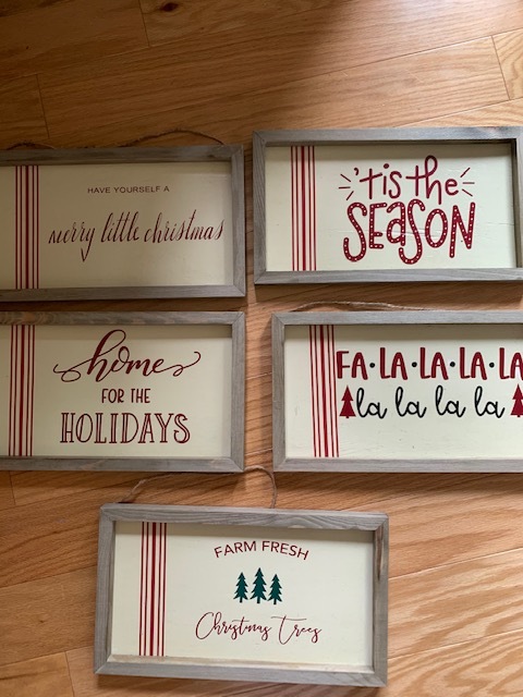 Five wooden signs reading Have Yourself a Merry Little Christmas, Tis the Season, Home for the Holidays, Fa La La La La La La La La, and Farm Fresh Christmas Trees.