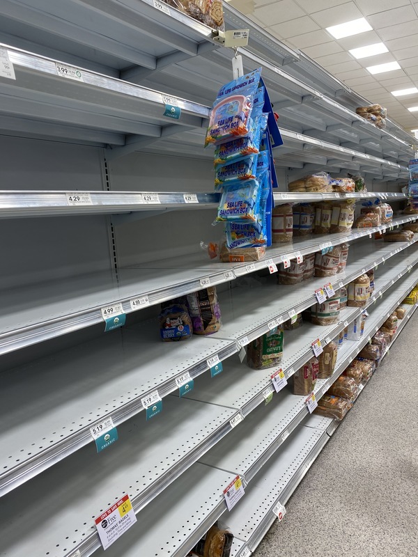 A bread aisle in a grocery store with a few loaves of bread left on the shelves.