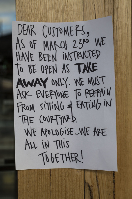 A piece of paper is taped up on a wooden door telling patrons that their store will be take out only and to refrain from sitting or eating in the courtyard.