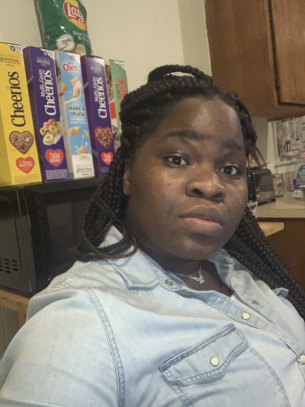 Photo of a woman sitting with boxes of cereal behind her.