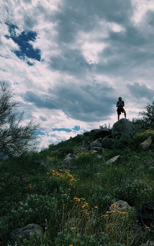 A person standing on top of a grassy hill in front of a cloudy blue sky.