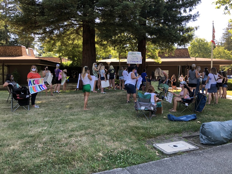 This is a picture taken of a group of people holding signs and protesting. Many are wearing face masks.