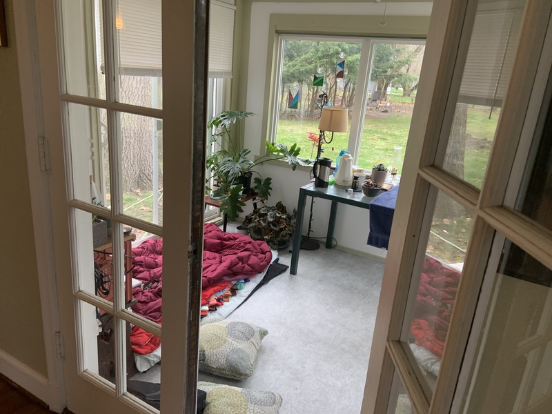 In a room full of windows is a sleeping cot on the floor.