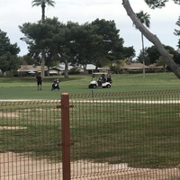 A golf course that has someone golfing while two people look on while sitting in a white golf cart.