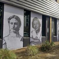 This is a picture taken of a series of murals that are painted on the side of a building. Various women in different periods of clothing are depicted in black and white. 