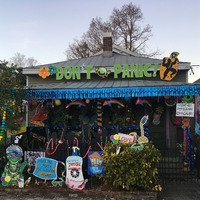 This is a picture taken of a person's house that has been decorated with various COVID-19 related messages or symbols. Some signs depict a container of hand sanitizer or a face mask, while a banner hanging from the roof reads "Don't Panic."