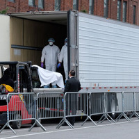 This is a picture taken of a refrigerated cadaver truck, with healthcare workers working carefully to use a forklift to deposit the remains of those who die from COVID-19.