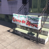 Sign attached to the railings in front of the steps leading up to double doors with text, "Cinco de Mayo" but "Mayo" is crossed out and "Lindsay" is written on the sign.