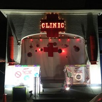 This is a picture of a building that has signs reading "clinic" attached to the front of it. A Red Cross flag is covering the entrance to the building, and small objects resembling COVID-19 particles hang in front of the flag.