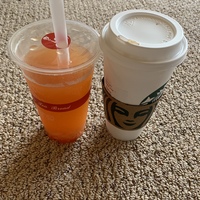 This is a picture of an orange drink set next to a Starbucks coffee cup.