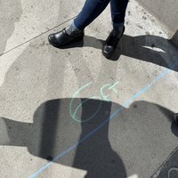 A sidewalk has measurements drawn on it with chalk to indicate 6 feet of distance for social distancing.