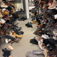 This is a picture taken of a messy footwear isle at a store. Shoes lie strewn across the ground of the isle.