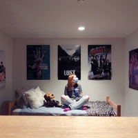 This is a picture taken of a girl sitting in her room, wearing a face mask.