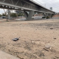 This is a picture of a face mask that has been discarded underneath a bridge in the dirt.