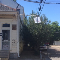Corner of a street with an older house with a sign in the door with text, "BALANCE? Where's The Fairness?" with a photo of a scale and it tipping to one side. Another sign hanging from a pole with text, "How Many Thousands More Americans Will Die....Due to Trump's Horrific Arrogance?"
