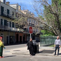 Three people are standing six feet apart from each other on the corner of a stop sign.